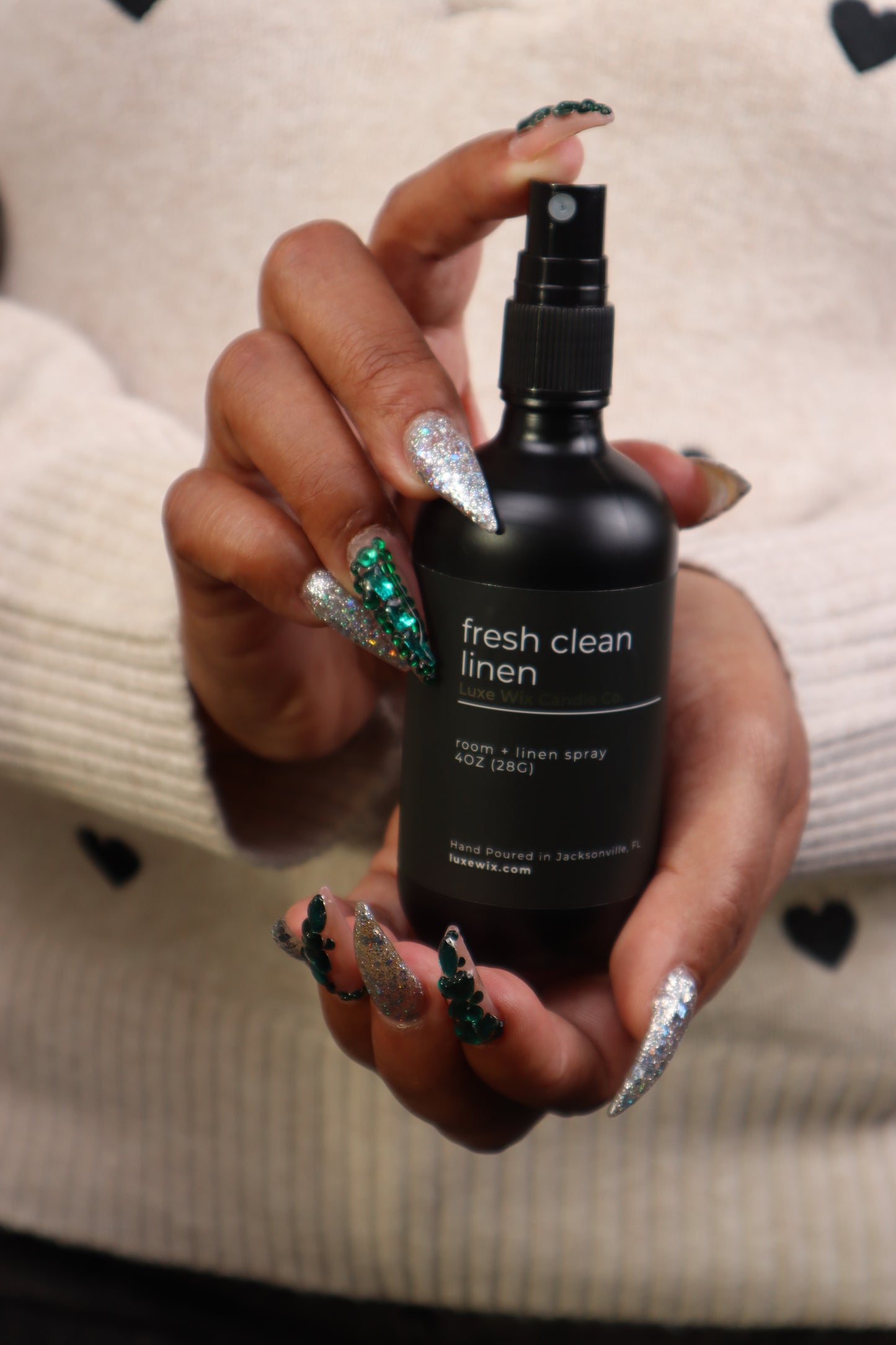 Hand holding a black bottle labeled 'fresh clean linen' with decorative nails.