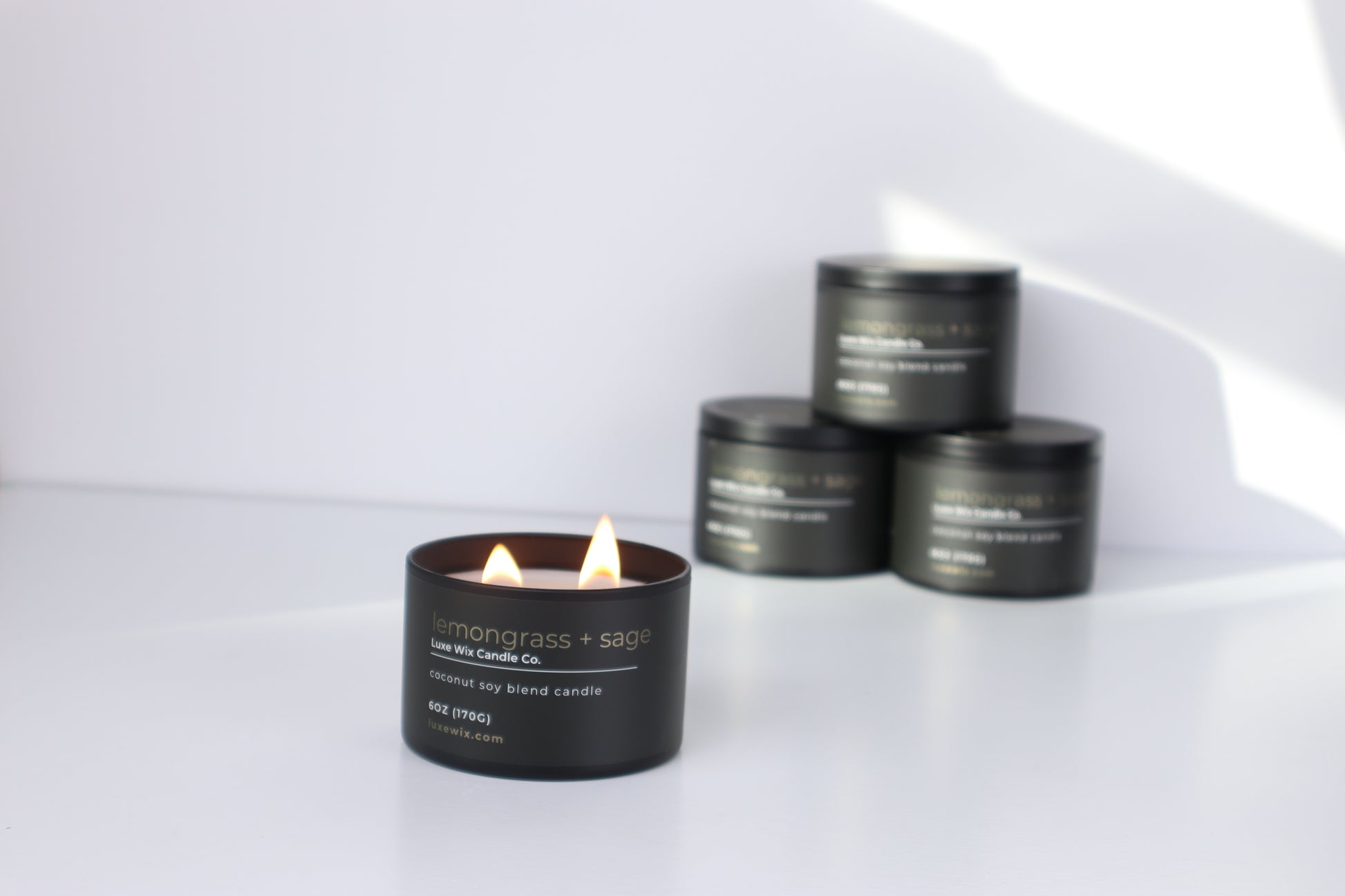 Black candle with visible flame on a white surface, surrounded by black containers.