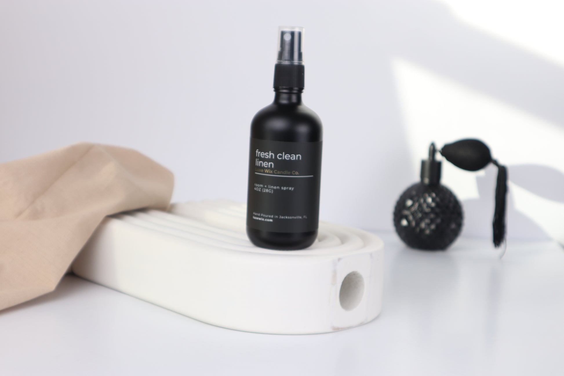 Black spray bottle labeled 'fresh clean linen' on a white surface with a beige cloth and black brush.